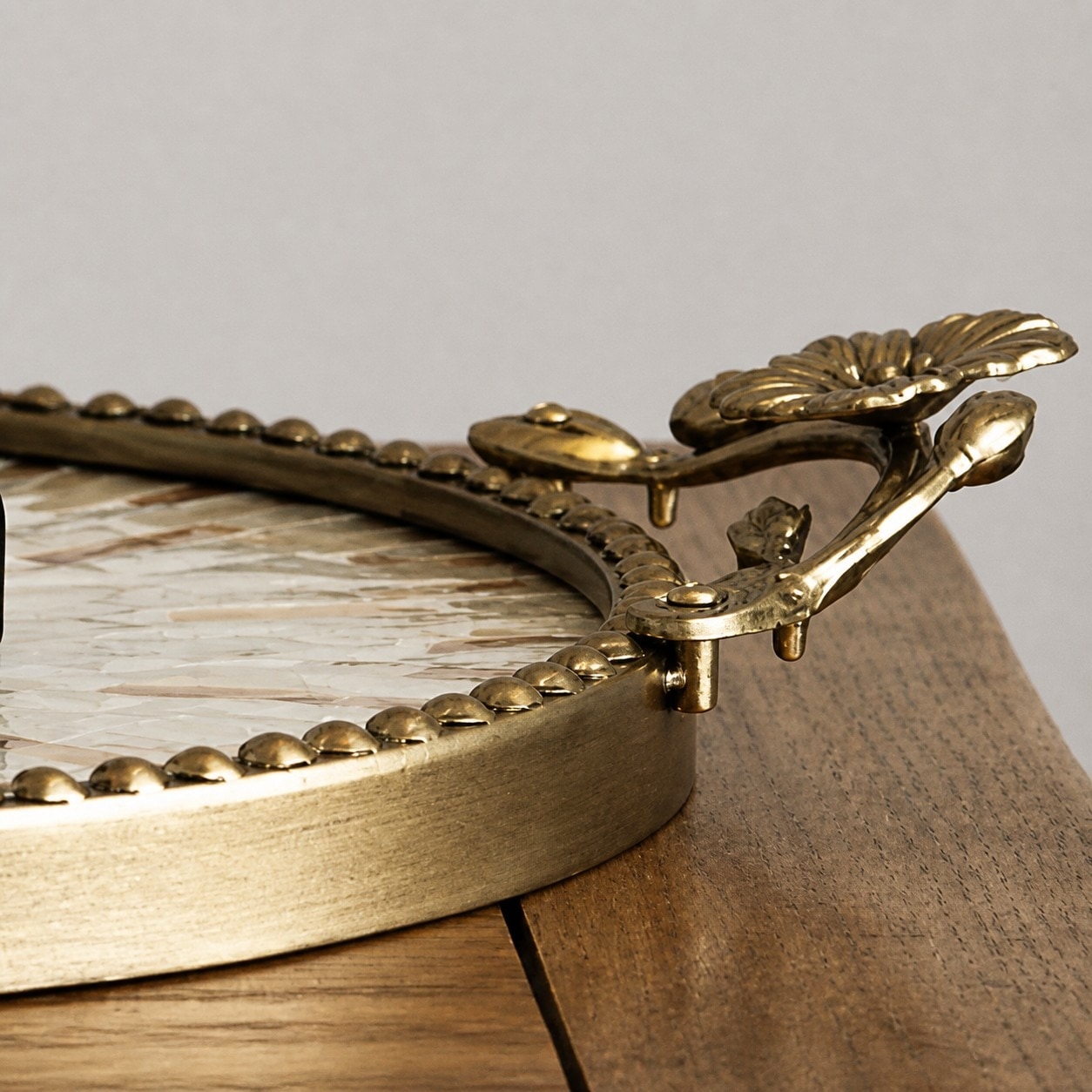 Raised antique brass rim and floral handle detail on round shell tray