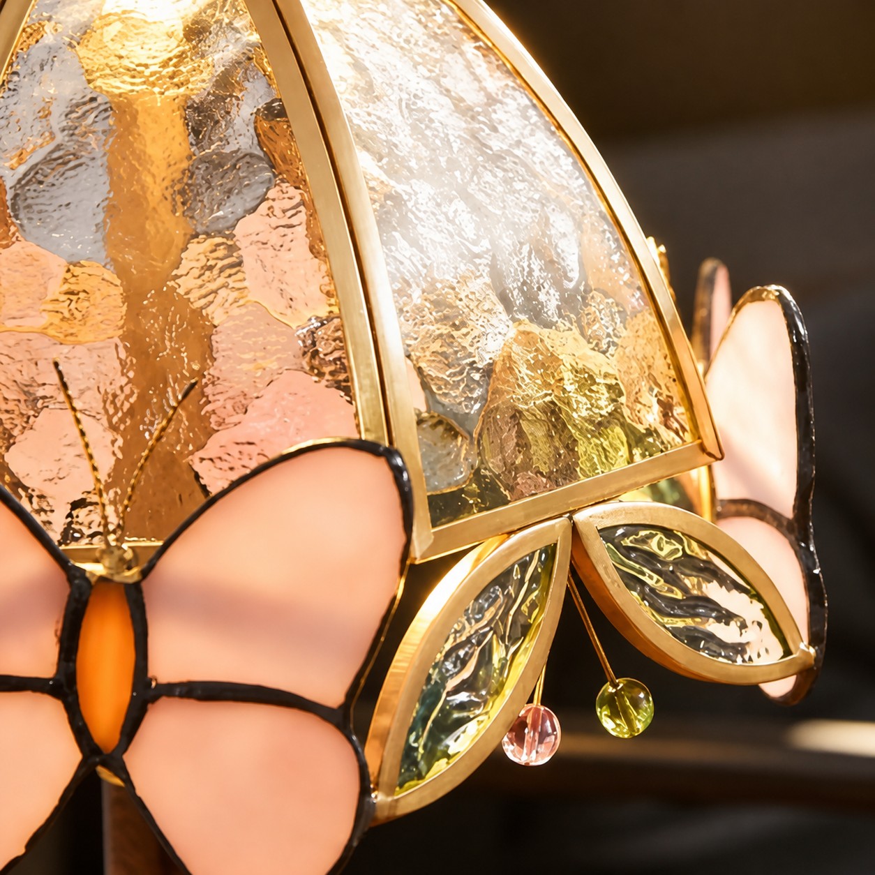 Close view of the hammered glass shade, brass frame, pink butterfly wings, and hanging glass beads
