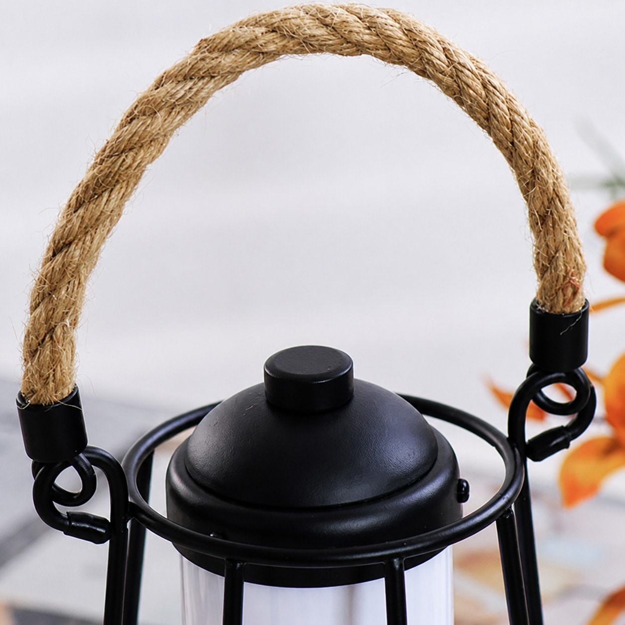 Lámpara de mano portátil con asa de cuerda y detalle superior de metal negro.